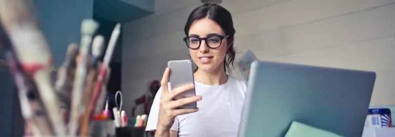 Persoon werkt op laptop en kijkt op telefoon.