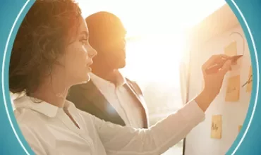 Two people at a board with sticky notes in sunlight.