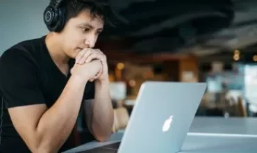 Persoon met koptelefoon kijkt naar laptop in moderne ruimte.